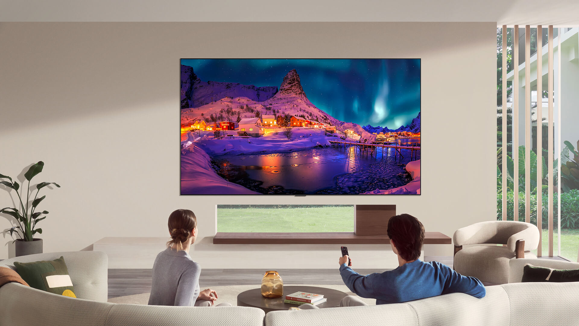 LG OLED evo AI G6 está montado al ras de la pared en una sala de estar moderna y muestra una vívida aurora sobre un pueblo costero nevado mientras un hombre y una mujer miran desde el sofá con un control remoto en la mano.